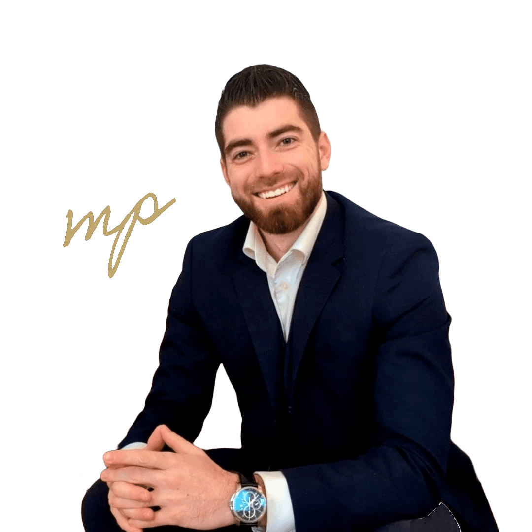 Smiling man with a beard wearing a navy suit, sitting with hands clasped together.