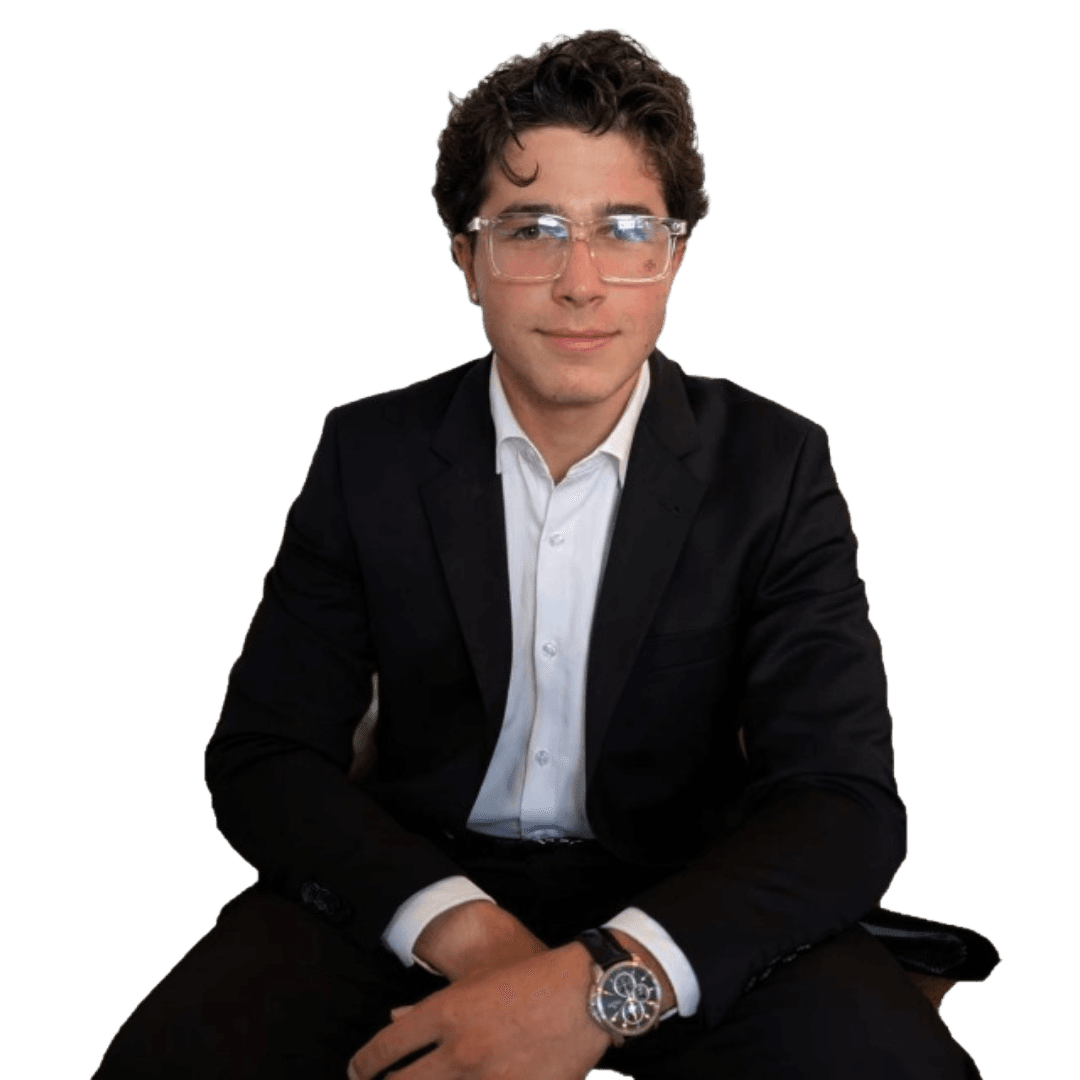 Young man with curly hair and clear glasses wearing a black suit against white background.